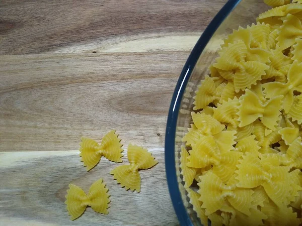 Pasta in the form of bows in a glass container on a wooden background — Stock Photo, Image