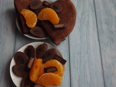 Çikolatalı krepli tatlı, mavi ahşap arka planda mandalina dilimli çikolata.
