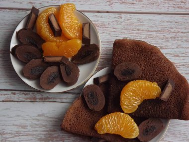 Çikolatalı krepli tatlı, mavi ahşap arka planda mandalina dilimli çikolata.