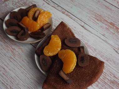 Çikolatalı krepli tatlı, mavi ahşap arka planda mandalina dilimli çikolata.