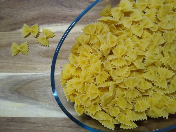 Macarrão na forma de arcos em um recipiente de vidro em um fundo de madeira — Fotografia de Stock