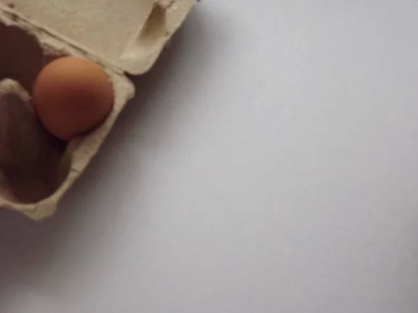 beige boiled eggs in a pot of water with an egg box on a gray background