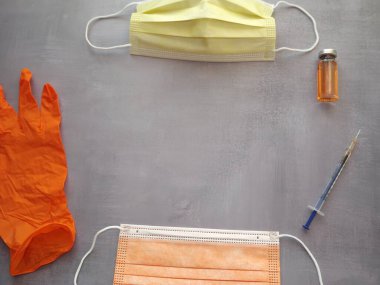 Gri arka plan, aşı, şırınga, turuncu tıbbi maske ve eldivenler.