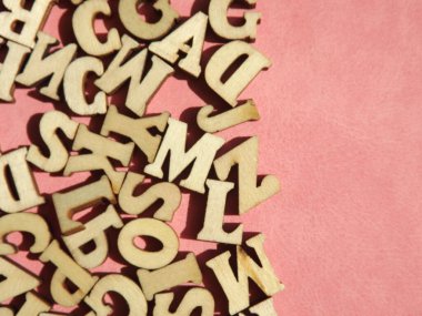 Arkaplan olarak pembe süet üzerine İngiliz alfabesinin ahşap harfleri