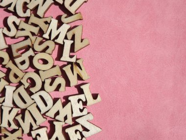 Arkaplan olarak pembe süet üzerine İngiliz alfabesinin ahşap harfleri
