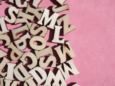 Arkaplan olarak pembe süet üzerine İngiliz alfabesinin ahşap harfleri