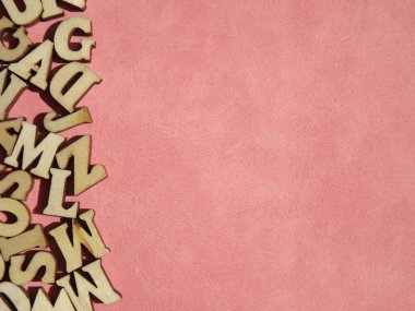 Arkaplan olarak pembe süet üzerine İngiliz alfabesinin ahşap harfleri