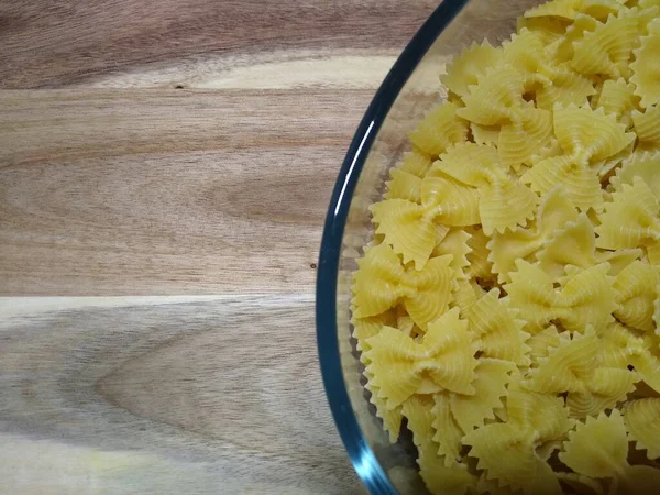 Macarrão na forma de arcos em um recipiente de vidro em um fundo de madeira — Fotografia de Stock