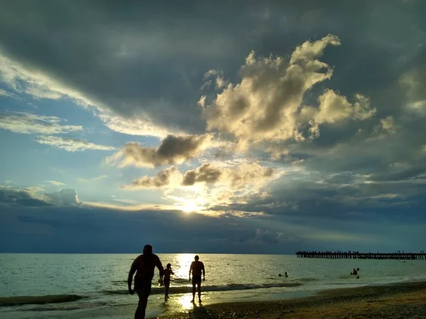 Мужчины и женщины отдыхают на пляже и купаются в море на закате Стоковая Картинка