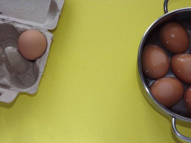 Gri arka planda yumurta kutusuyla su dolu bir tencerede bej kaynamış yumurta.