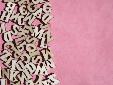 Arkaplan olarak pembe süet üzerine İngiliz alfabesinin ahşap harfleri