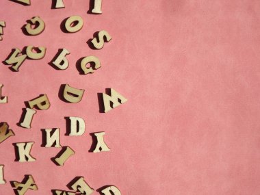 Arkaplan olarak pembe süet üzerine İngiliz alfabesinin ahşap harfleri
