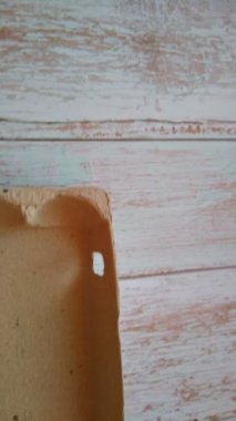 Bir kadının eli yumurta kutusundan bej bir yumurta alır.