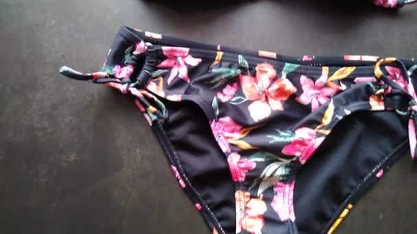 Układ bikini damskiego, czarny strój kąpielowy z kwiatowym wzorem na szarym tle — Wideo stockowe