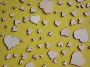 Sarı arka planda farklı boyutlarda tahta kalpler. Sevgililer Günü, bir aşk ilanı