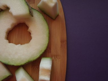 Olgun kavun tahta üzerinde dilimler halinde kesilmiş.