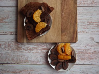 Çikolatalı krepli tatlı, mavi ahşap arka planda mandalina dilimli çikolata.