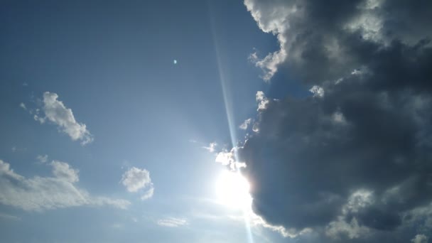 In een blauwe hemel komt de zon van achter een wolk. — Stockvideo