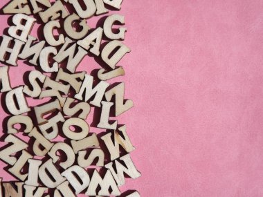 Arkaplan olarak pembe süet üzerine İngiliz alfabesinin ahşap harfleri