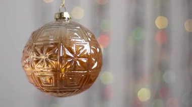 Güzel Noel ağacı oyuncağı çok renkli Noel ışıklarının arka planında asılı ve hafifçe hareket ediyor. Yakın plan. Kürenin şeklindeki Noel ağacı oyuncağı, şeffaf..