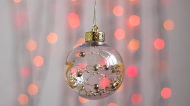 Güzel Noel ağacı oyuncağı çok renkli Noel ışıklarının arka planında asılı ve hafifçe hareket ediyor. Yakın plan. Altın yıldızlı ve bal rengi küreli şeffaf Noel ağacı oyuncağı