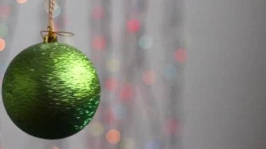 Güzel Noel ağacı oyuncağı çok renkli Noel ışıklarının arka planında asılı ve hafifçe hareket ediyor. Yakın plan. Parıltılı yeşil bir küre şeklinde Noel ağacı oyuncağı. amera Taşıyıcıları