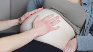 Genç, gelecekteki anne ve baba hamile ve çıplak bir göbeği okşuyor. Yakın plan. Şefkatli ve sevgi dolu ebeveyn kavramı.