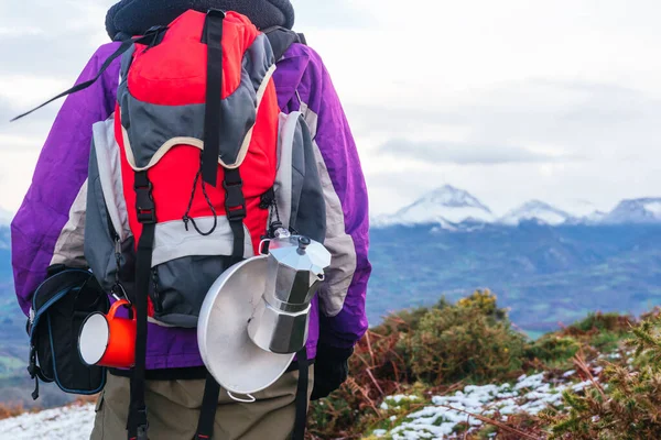 detail of an unrecognizable camper\'s backpack. red backpack with camping utensils in the background a landscape of snowy mountains.