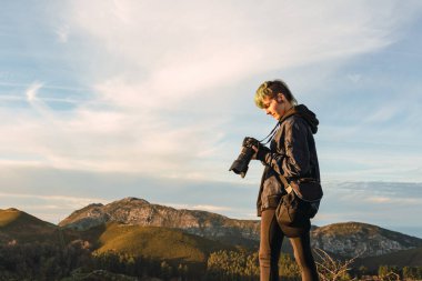 Genç profesyonel fotoğrafçı punk stili resimlerini gözden geçiriyor. Gün batımında dağlarda bir iş gününde..