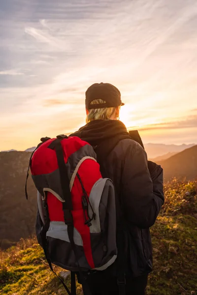 Traveler woman with backpack looking at an inspiring sunset during her hike up the mountain.