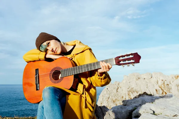 Gitarına yaslanmış sakin genç bir kadın uçurum kenarında düşünceli bir jestle. Yolculuk tutkusu