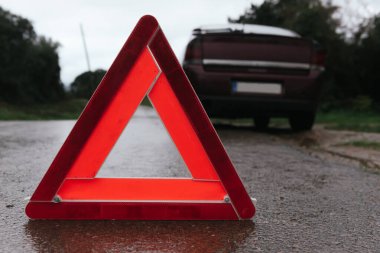 red warning triangle on the road in front of a broken car clipart