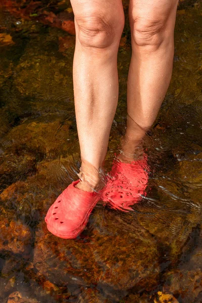 Legs of an unrecognizable older woman in rubber sandals refreshing the feet in the water of a river one summer day. and summer time and vacation. retirement.