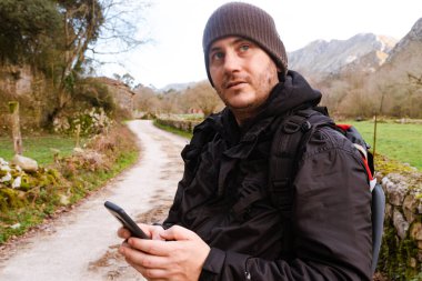 Sırt çantalı bir adam kaybolma jesti yapıyor, akıllı telefonuna yol hakkında danışmanlık yapıyor. dağ ve spor.