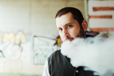 Kafkasyalı beyaz adam buharlaşırken kameraya bakıyor. Sigarayı bırakan kişi. Elektronik bir sigara yüzünden oluşan buhar bulutları. Sorunlu banliyöde bir çocuk.