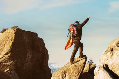 Dağda bir kayanın üzerinde duran yürüyüşçü, yumruğunu kaldırıyor ve barış bayrağı taşıyor. Spor ve kapsama. Barış için savaşıyorum. Dağları seyreden dağcı..