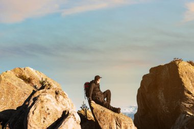 Sırt çantalı bir yürüyüşçü bir kayanın üzerinde dinleniyor. Dağcı gün batımında manzarayı seyrediyor. Hafta sonu kaçamağı. dağ sporları ve aktiviteleri