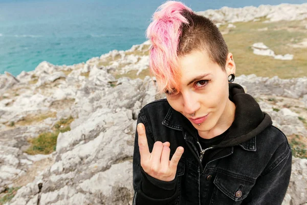 Oturan punk kadının dikey portresi dilini çıkarıp rock 'n roll işareti yapıyor. Heavy metal ve ekstrem müzik. punk rock. şehir kabileleri.