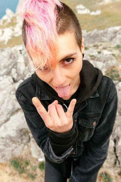 Vertical portrait of sitting punk woman sticking her tongue out and performing the rock and roll sign. Heavy metal and extreme music. punk rock. urban tribes.