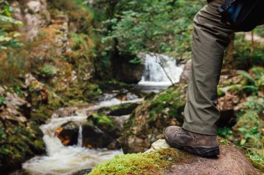 Nehrin yukarısındaki bir kayanın üzerinde yürüyüş ayakkabısı. Manzarayı izleyen tanınmamış bir yürüyüşçü. dağ aktiviteleri ve aktif turizm. macera konsepti.