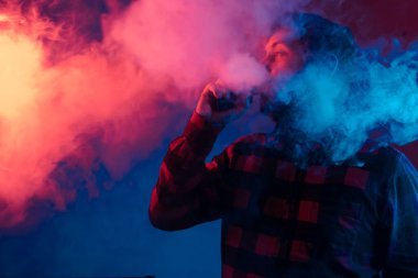 Stüdyoda renkli ışıklarla buharlaşan yetişkin biri. Elektronik sigara kullanan ve yüksek miktarda buhar çıkaran bir adam. Neon ışıkları olan teneke çocuk. Tütüne alternatif