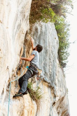 İp, koşum takımı ve kancalarla dağdaki dik kaya duvarına tırmanan bir adamın dikey fotoğrafı. dağ sporları ve macera