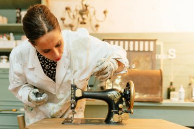 young Hispanic woman working in her carpentry shop. person restoring and painting old sewing machine. craftswoman.