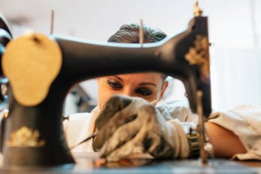 smiling woman painting and restoring old sewing machine in her workshop. Arts and crafts.