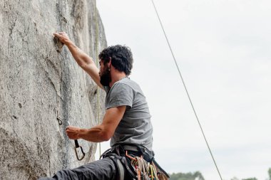 Genç bir çocuk, dağlara tırmanırken kayaya kancalarla tutunuyor. Adam tırmanıyor ve duvara tırmanıyor.