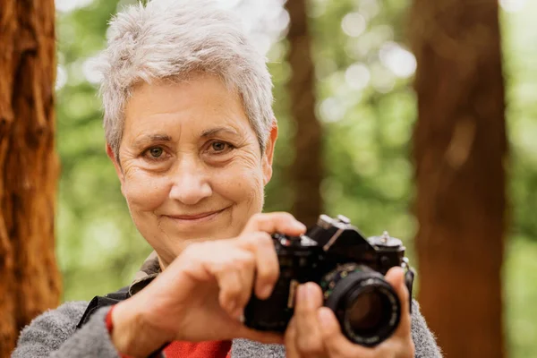 70 yaşındaki yaşlı bir kadının, kameraya bakıp elinde bir fotoğraf makinesi tutarken çekilmiş bir portresi. Emekli maceracı