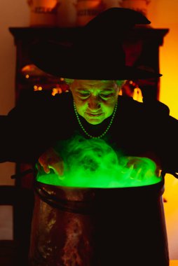 Cadılar bayramında cadı kılığına girmiş yaşlı kadın iksirini gözlemliyor..