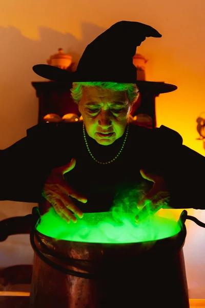 古老的经典女巫看着她的魔法壶里面散发着绿光和烟雾 老年人庆祝圣餐日 — 图库照片