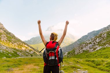 Kırmızı sırt çantalı beyaz bir kadın gün batımında bir vadi ve bir dağın önünde kollarını kaldırıyor. Hafta sonu kaçamağı ve doğada tatiller. Macera seyahatleri.