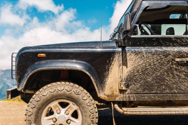 Dağ yolunda çamur ve toz lekesi olan siyah 4x4 off-road arabası